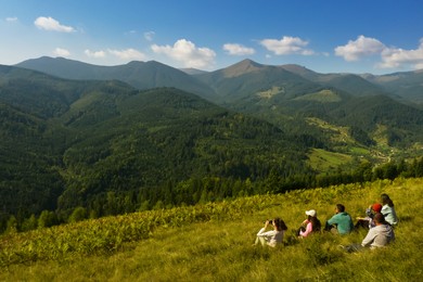 Image of Group of tourists sitting on hill in mountains