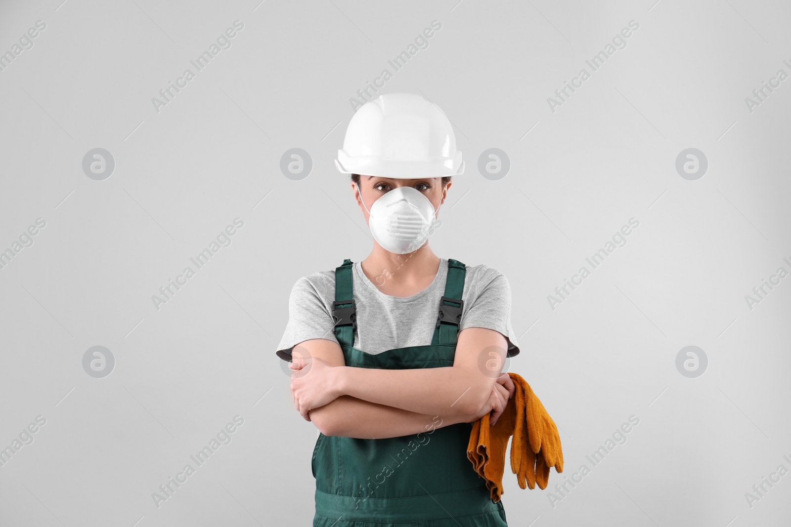 Photo of Female industrial worker in uniform on light background. Safety equipment