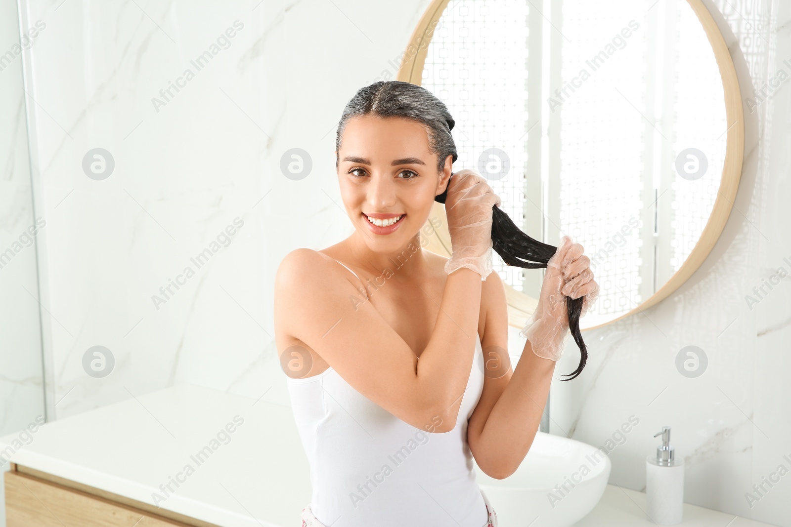 Photo of Young woman dyeing her hair in bathroom