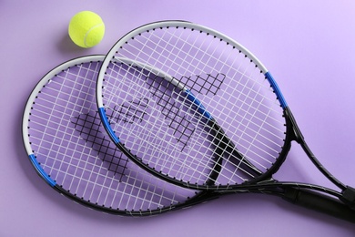 Tennis rackets and ball on violet background, flat lay. Sports equipment
