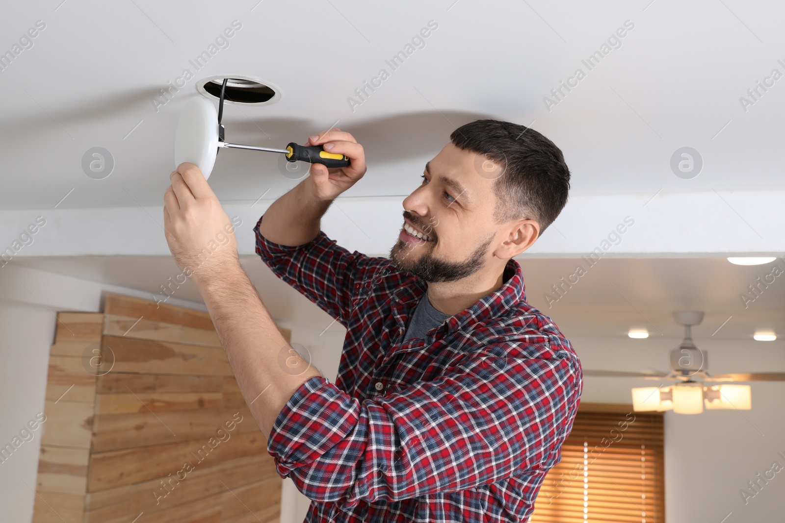 Photo of Man with screwdriver repairing ceiling lamp indoors