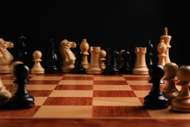 Photo of Many chess pieces on wooden checkerboard against black background, selective focus