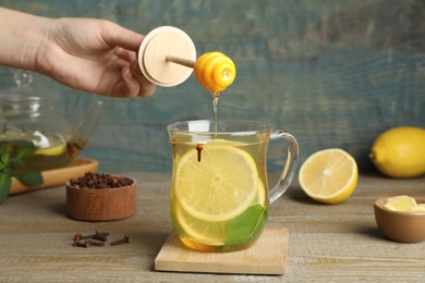 Photo of Woman adding honey to immunity boosting drink at wooden table, closeup