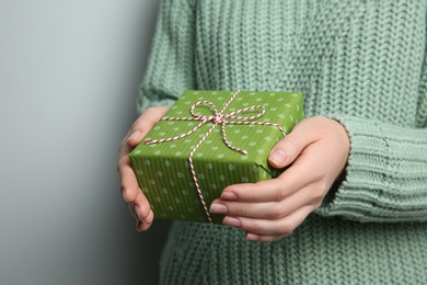 Photo of Woman holding green Christmas gift box on grey background, closeup