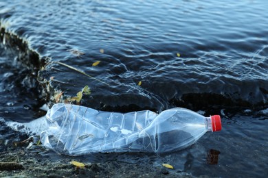 Photo of Used plastic bottle near water outdoors. Environment pollution