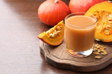Photo of Tasty pumpkin juice in glass, whole and cut pumpkins on wooden table. Space for text