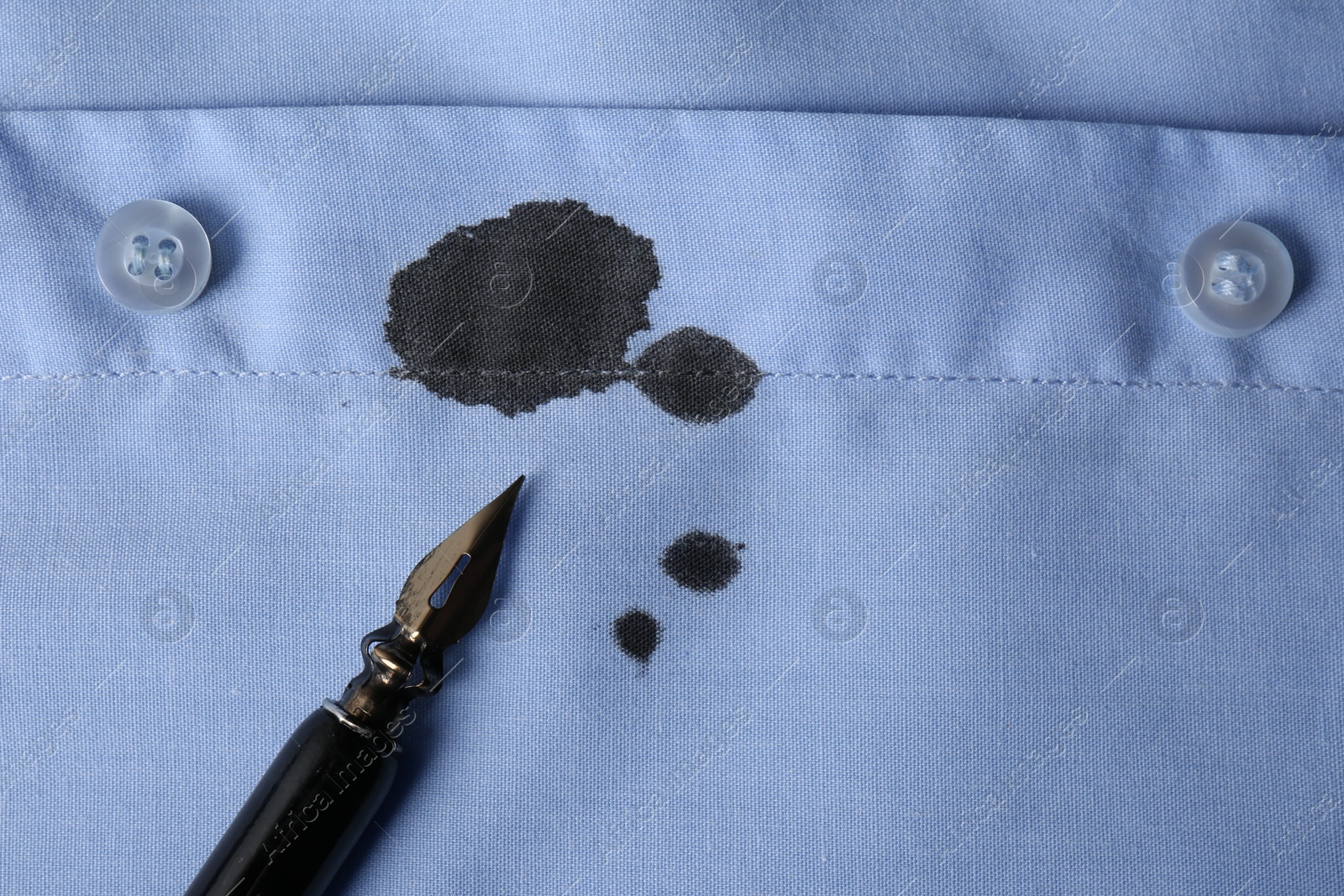 Photo of Black ink stain on light blue shirt and pen, top view. Space for text