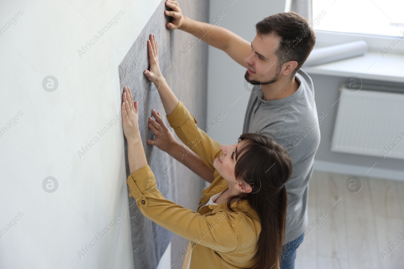 Photo of Couple hanging stylish gray wallpaper in room