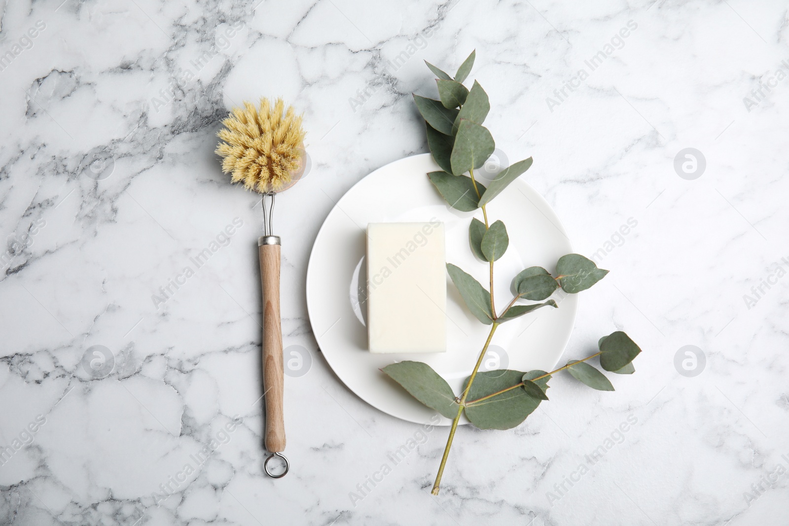 Photo of Cleaning supplies for dish washing, plate and eucalyptus branch on white marble table, flat lay