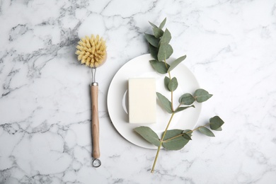 Photo of Cleaning supplies for dish washing, plate and eucalyptus branch on white marble table, flat lay