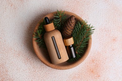 Photo of Bowl with bottles of aromatic essential oil, pine branches and cone on color table, top view