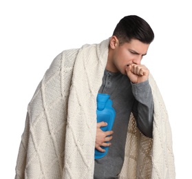 Photo of Ill man with hot water bottle and knitted blanket coughing on white background