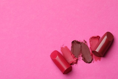 Photo of Different lipsticks and smears on pink background, flat lay. Space for text