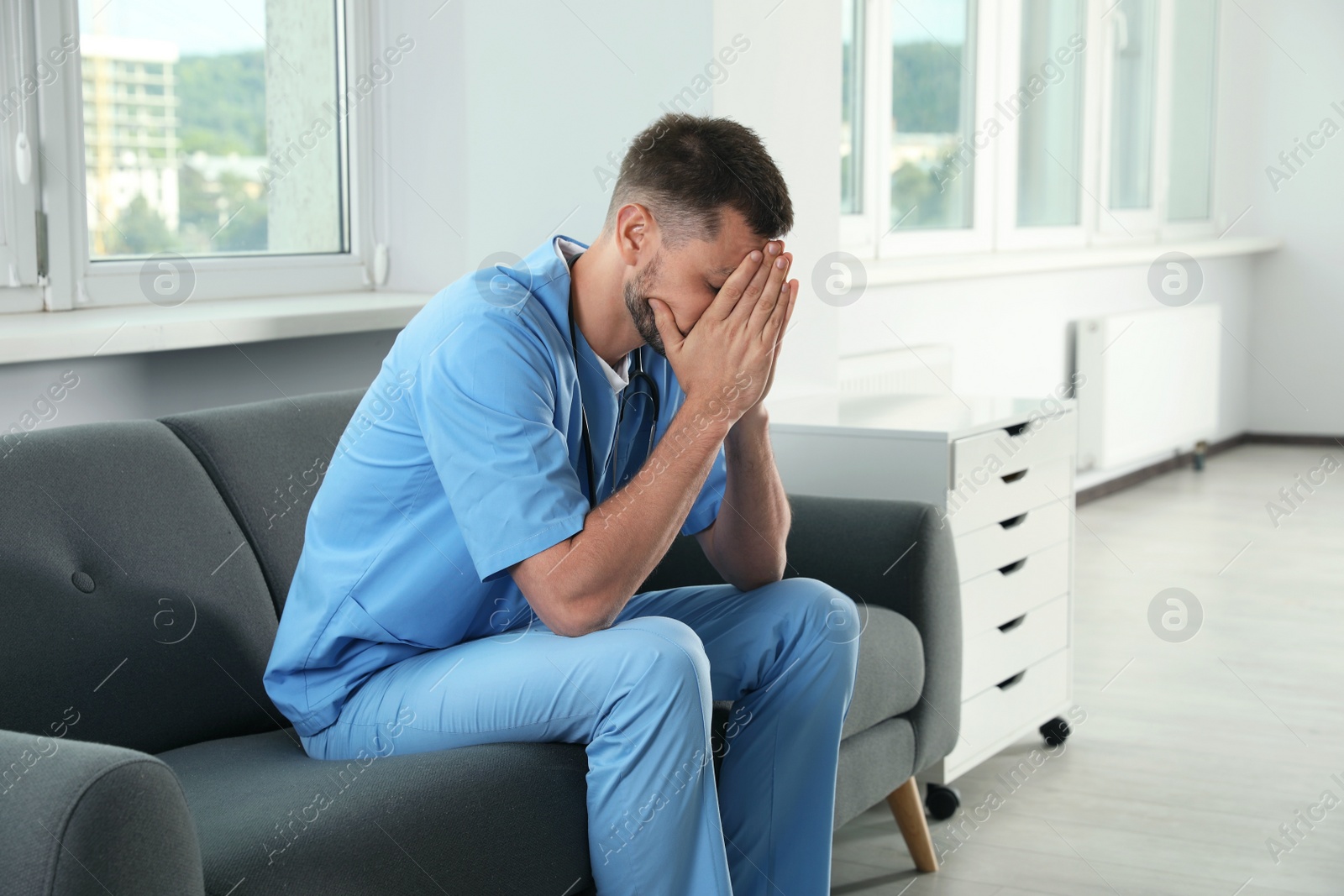 Photo of Exhausted doctor covering face on sofa in hospital