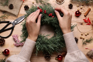 Photo of Florist making beautiful Christmas wreath with berries at wooden table, top view