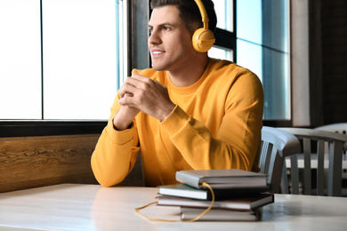 Photo of Man with headphones connected to book at table in cafe