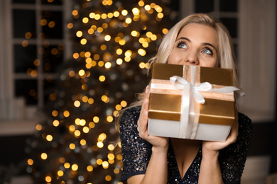 Beautiful woman with gift box near Christmas tree at home