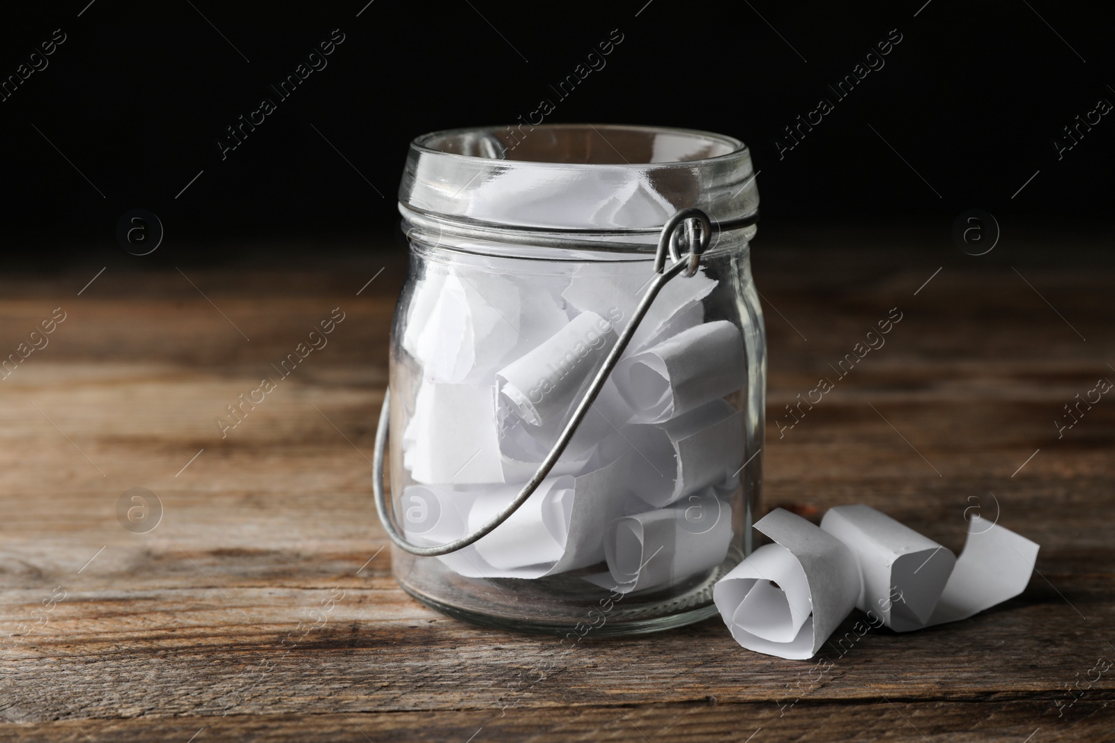 Photo of Glass jar with paper pieces on wooden table