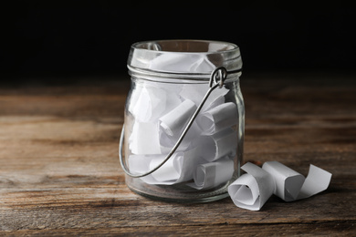 Glass jar with paper pieces on wooden table