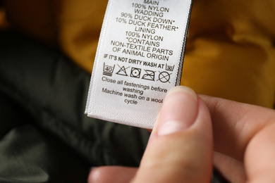 Photo of Woman reading clothing label with care symbols and material content on color jacket, closeup