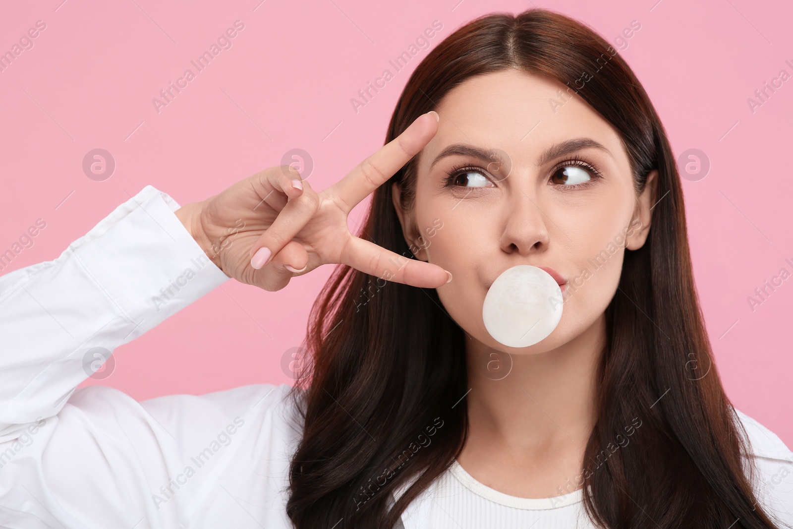 Photo of Beautiful woman blowing bubble gum and gesturing on pink background