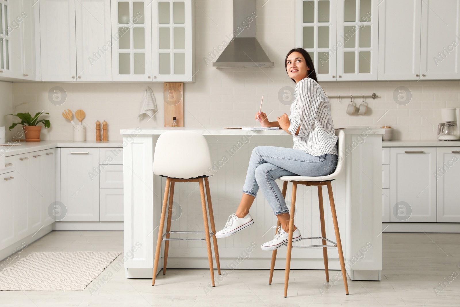 Photo of Beautiful young woman with notebook sitting on stool in kitchen