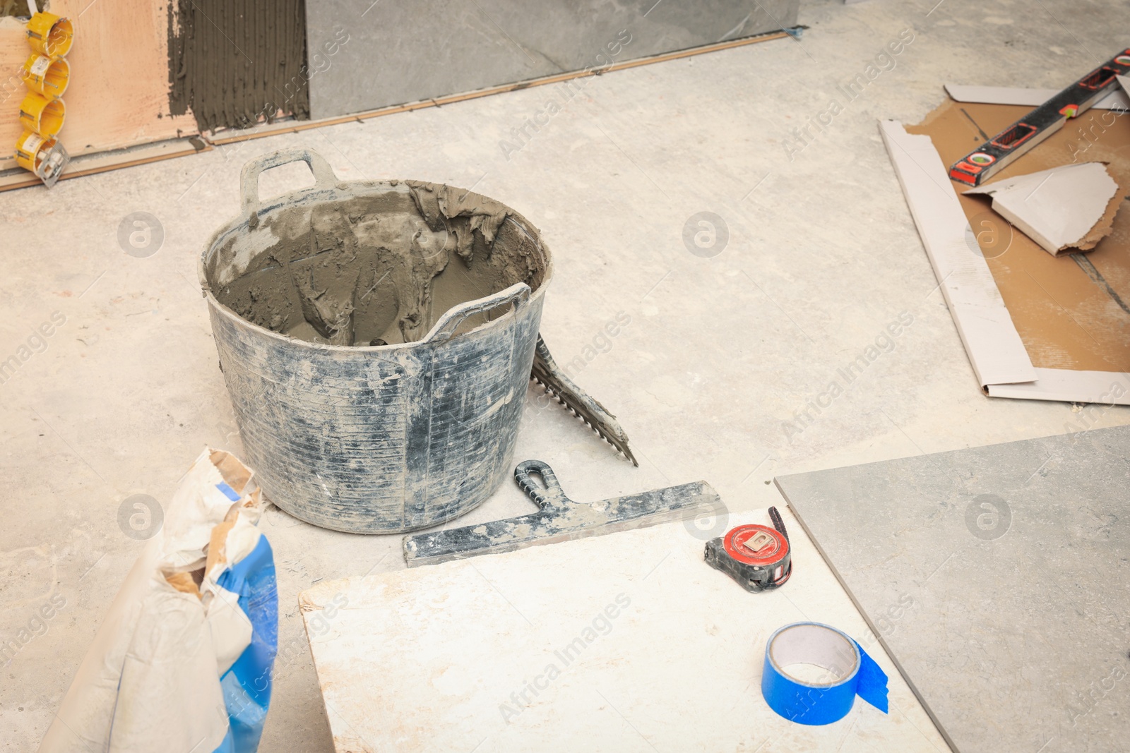 Photo of Bucket of adhesive mix and different tools on floor indoors. Tile installation process