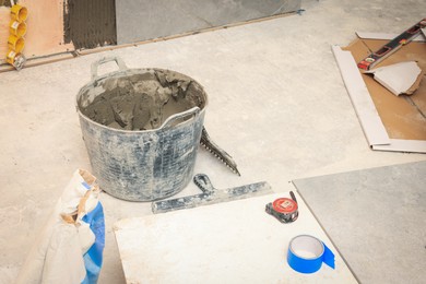 Bucket of adhesive mix and different tools on floor indoors. Tile installation process