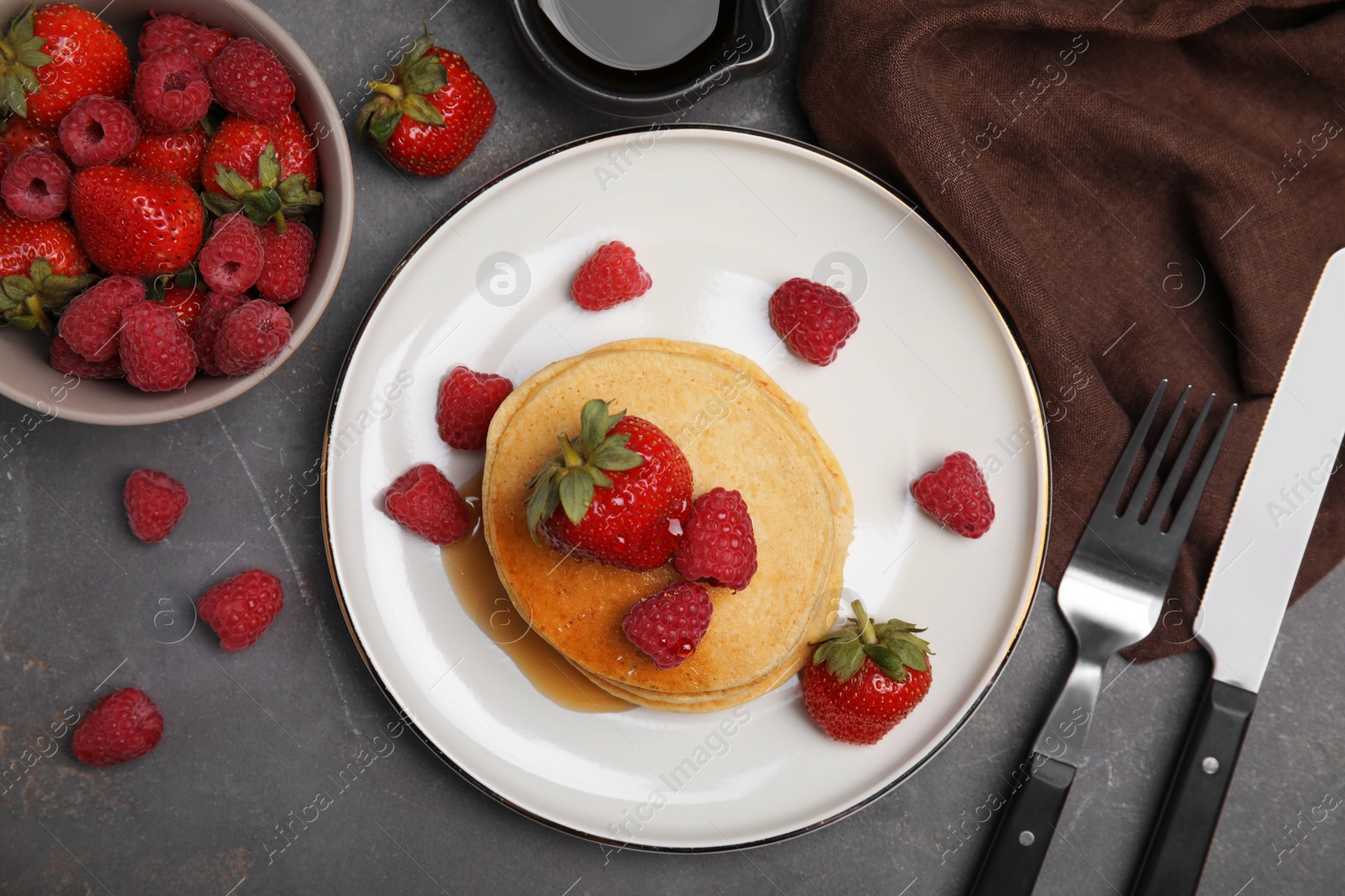 Photo of Tasty pancakes served with fresh berries and honey on grey table, flat lay