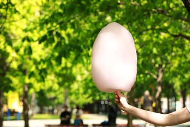 Photo of Woman holding sweet cotton candy in park, closeup. Space for text