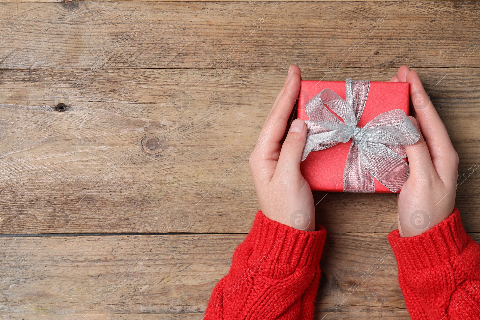 Photo of Christmas present. Woman holding gift box at wooden table, top view. Space for text