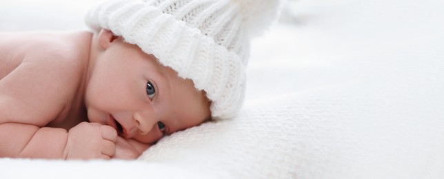 Image of Cute newborn baby in white knitted hat on plaid, closeup view with space for text. Banner design