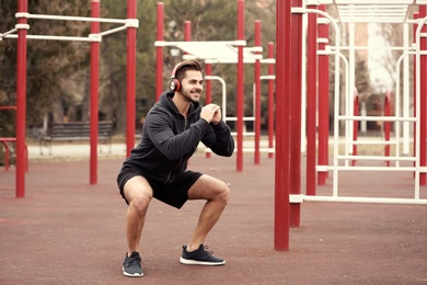 Photo of Young man with headphones listening to music and exercising on sports ground