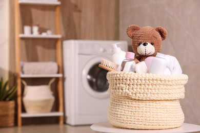 Photo of Knitted basket with baby cosmetic products, bath accessories and toy bear on white table indoors. Space for text