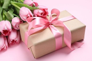 Photo of Beautiful gift box with bow and tulip flowers on pink background, closeup