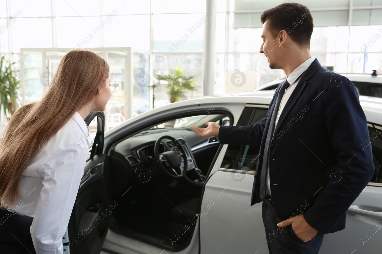 Photo of Young woman choosing new car with salesman in salon