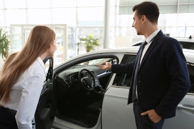 Young woman choosing new car with salesman in salon