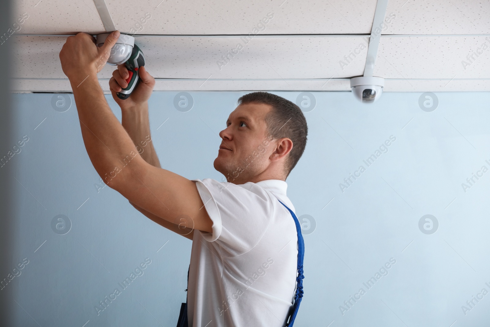 Photo of Technician installing CCTV camera on ceiling indoors