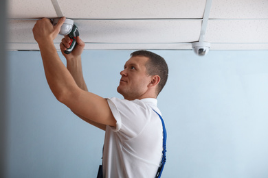 Photo of Technician installing CCTV camera on ceiling indoors