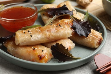 Photo of Tasty fried spring rolls, lettuce and sauce on grey table, closeup