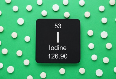 Card with iodine element and pills on green background, flat lay