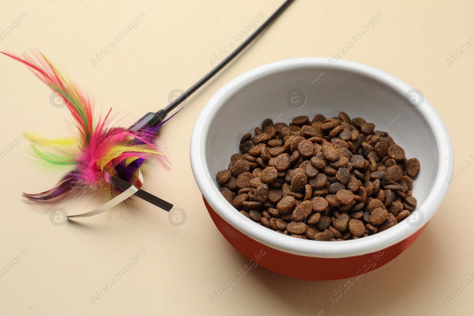 Photo of Dry cat food in bowl and pet toy on beige background