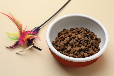 Photo of Dry cat food in bowl and pet toy on beige background
