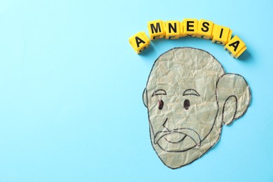 Photo of Yellow cubes with word Amnesia and human face made of crumbled paper on light blue background, top view. Space for text