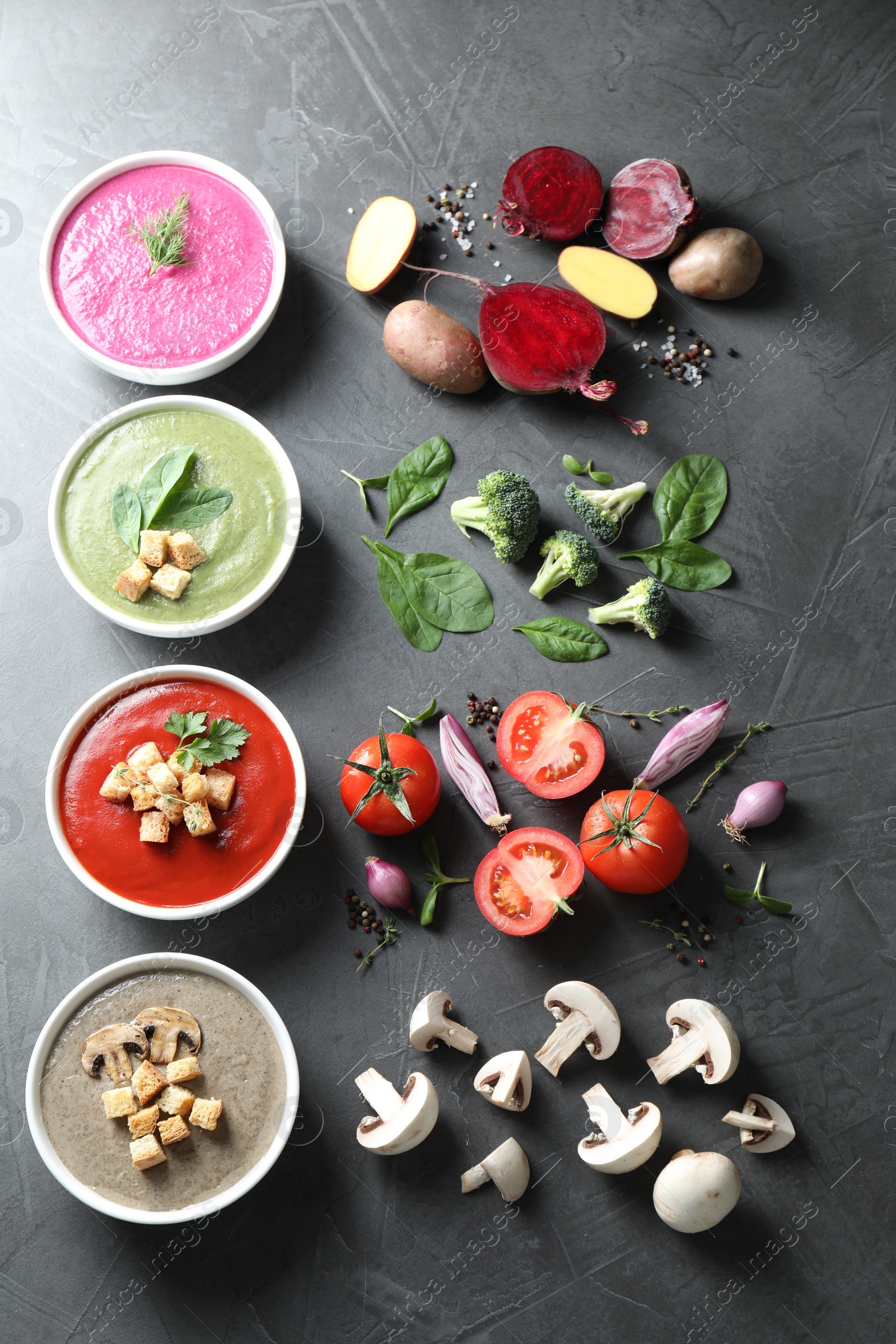 Photo of Different tasty cream soups in bowls and ingredients on dark grey table, flat lay