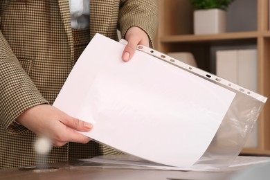 Businesswoman putting document into punched pocket in office, closeup