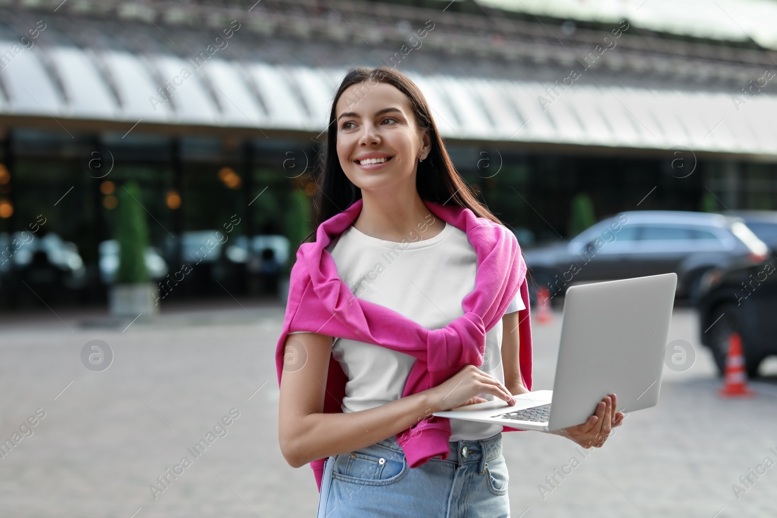 Photo of Happy young woman using modern laptop on city street