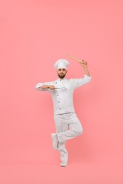 Photo of Professional chef holding kitchen utensils and having fun on pink background