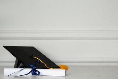 Graduation hat and diploma on floor near white wall, space for text
