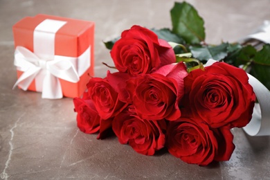 Photo of Beautiful red roses and gift box on grey table, closeup. Valentine's Day celebration